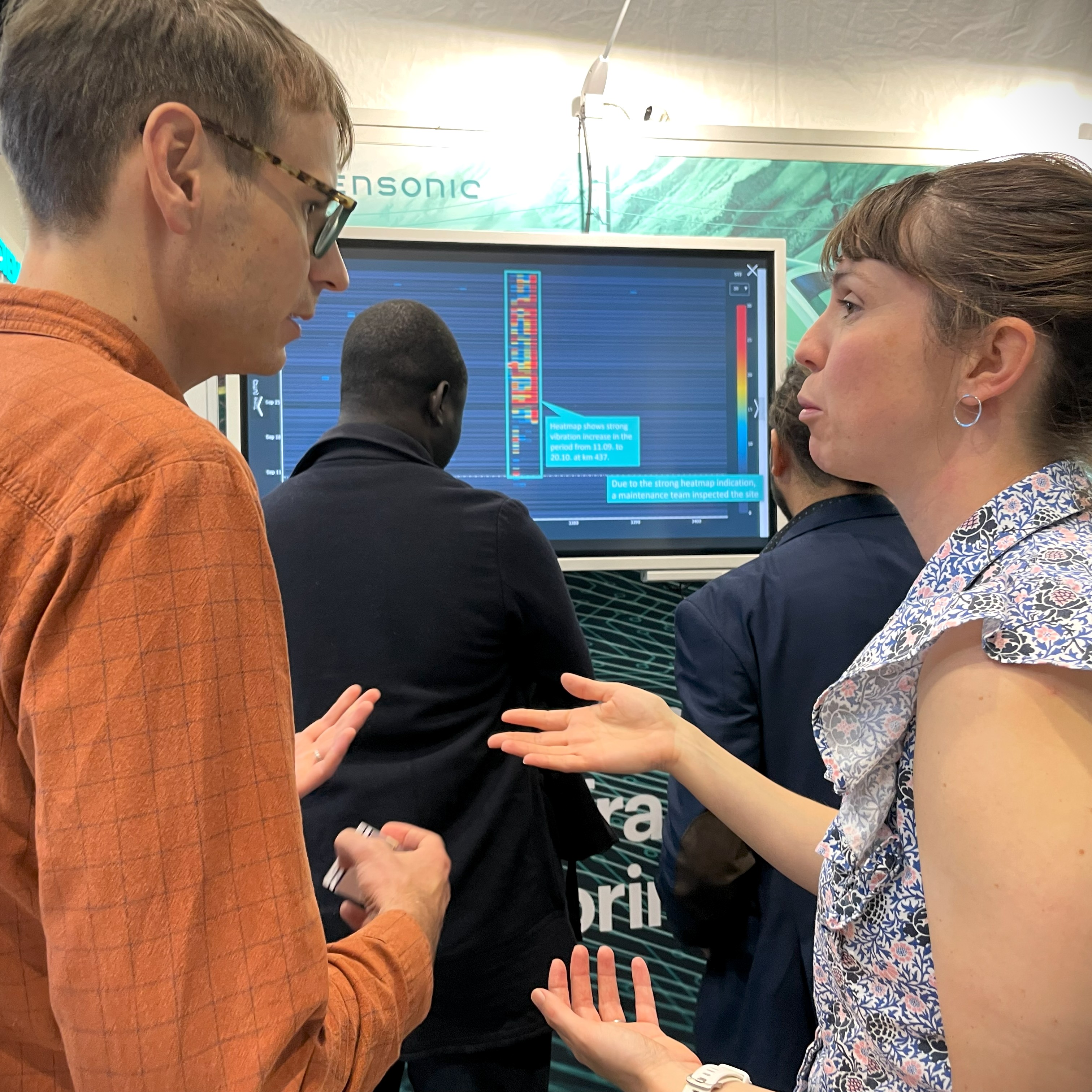 A lady and man talking infront of a screen. On the screen appears data from Sensonics Track Condition Monitoring application.