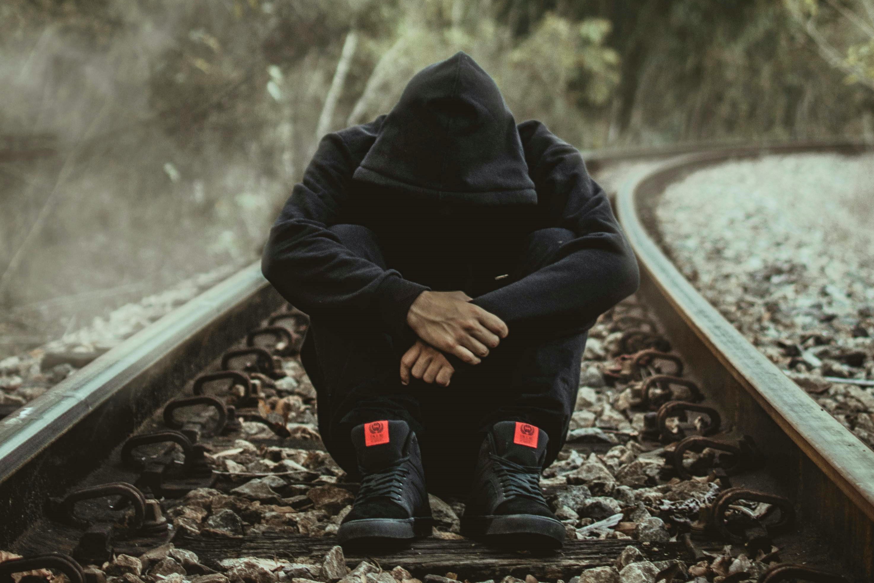 Someone sat on a railway track looking downward with their head covered. They appear to be contemplating suicide